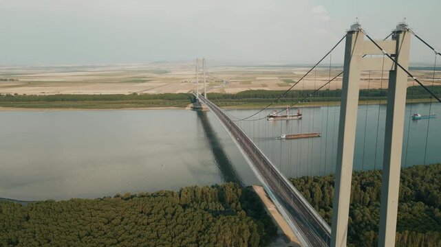 Aerial View Of Braila Bridge Spanning Danube River, Connecting Forested Bank To Open Farmland In Romania. ascending sideways shot