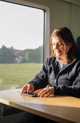 Woman typing on smartphone while riding a train through the countryside. Productive and relaxed...