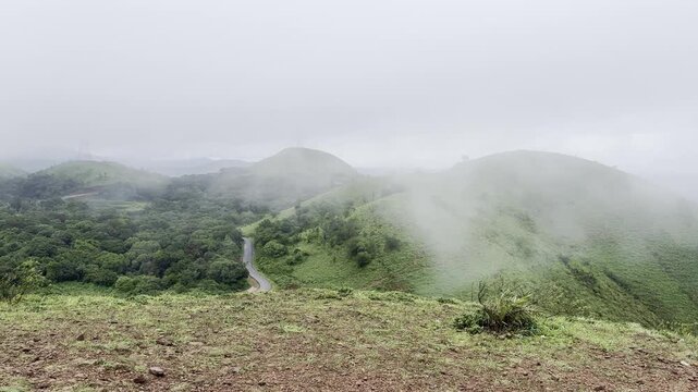 Rolling green mountains of Devarmane, Malnad, Karnataka during monsoon. Rain clouds sweep swiftly overhead, capturing the serene and dramatic beauty of the Western Ghats.