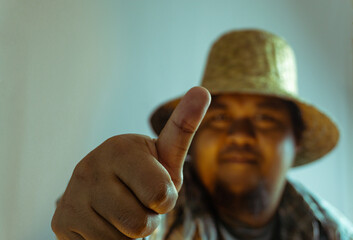 Farmer in straw hat giving thumbs up, face blurred and background white, positive rural gesture...