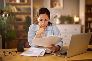 A woman sits at her home office desk in the afternoon, thoughtfully examining financial documents...