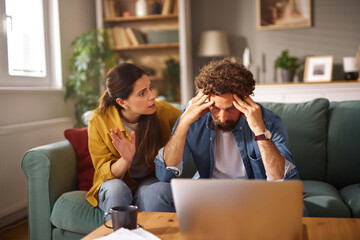 A man and woman are having a serious discussion about financial problems in a cozy living room. The...