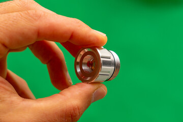 Frontal magnifying glass regulating laser light beam held between fingers on a green background.