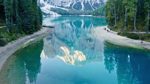 Aerial view of Lago di Braies displaying a stunning reflection of the snow-capped mountains and lush green trees in the crystal-clear turquoise water, Oberhaus, Trentino-South Tyrol, Italy.