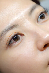 Young southeast asian woman undergoing an eyelashes extension procedure in beauty salon. calm...
