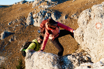 A fit and adventurous couple helps each other climb to the mountain summit during a breathtaking...