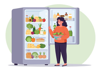 A woman stands in front of an open refrigerator, holding a bowl of salad, surrounded by fresh produce and food items.