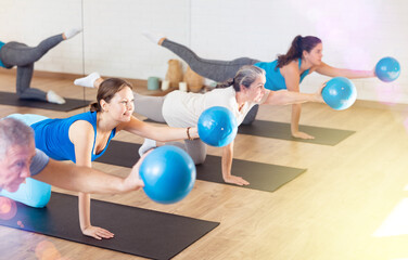 People of different ages stretching leg and arm, holding mini ball in their hands during Pilates...