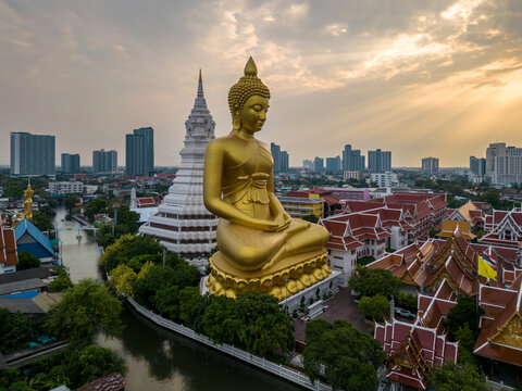 A boat was passing Big Buddha statue (Phra Buddha Dhammakaya Thepmongkhon ) in Wat Pak Nam Phasi Charoen temple located by the river during sunset.