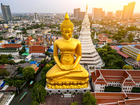A boat was passing Big Buddha statue (Phra Buddha Dhammakaya Thepmongkhon ) in Wat Pak Nam Phasi Charoen temple located by the river during sunset.