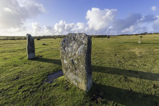 View of Hurlers Standing Stones rise majestically from the grassy plain under a vast blue sky dotted with fluffy white clouds, Minions, England, United Kingdom.