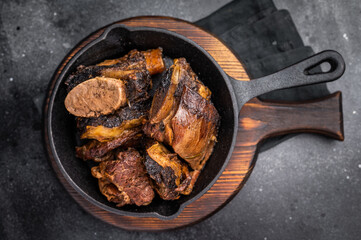 Tender beef short ribs in a pan, seasoned with herbs and spices. Perfect for culinary blogs or restaurant menus that focus on hearty, flavorful meat dishes. black background. top view
