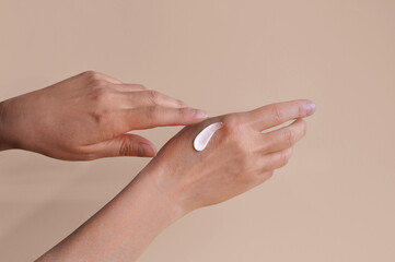 Woman's hand applying hand care cream on soft beige pink background. Female old hands with cosmetic cream. Hand cream - skin care concept. Close up. Moisturizing and hydrating. Beauty and spa routine.