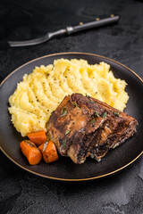 Braised beef short ribs resting on a bed of creamy mashed potatoes, creating an inviting culinary scene. black background. top view
