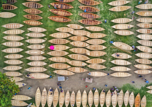 Aerial view of rows of wooden boats resting on the green grass, a pink umbrella standing out amid the earthy tones, creating a vibrant contrast, Dhaka, Bangladesh.