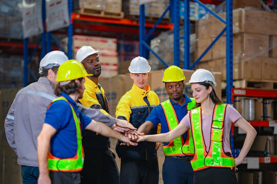 Workers in uniforms gather to form a team huddle in the warehouse. The gesture signifies shared vision, teamwork spirit, and effective coordination in a large-scale logistics operation.