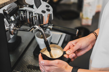 Barista frothing milk with a steam wand at a coffee shop, captured in a close-up showing hands,...
