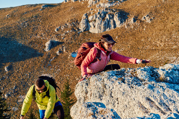 A fit and adventurous couple helps each other climb to the mountain summit during a breathtaking...