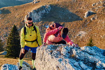 A fit and adventurous couple helps each other climb to the mountain summit during a breathtaking...