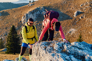 A fit and adventurous couple helps each other climb to the mountain summit during a breathtaking...
