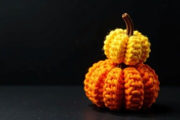 A charming autumnal display featuring a handcrafted, two-tiered pumpkin decoration, meticulously crocheted from vibrant orange and yellow yarn, rests elegantly on a dark surface.