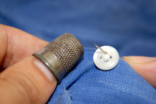 Male hand sewing a button onto a shirt with a thimble - Powered by Adobe
