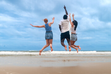 Rear view happy young teenagers jumping on the beach on summer vacation