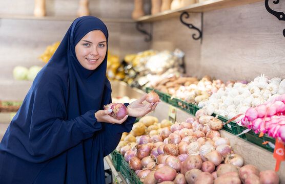 Portrait of female customer in paranja selecting onion in grocery