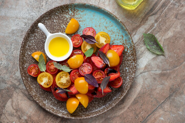 Plate with freshly made strawberry, tomato and basil salad on a brown granite background, horizontal shot, flat lay