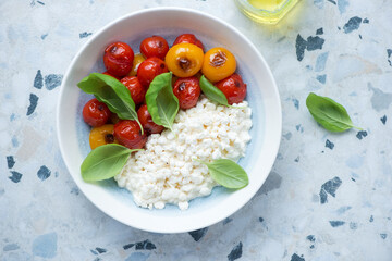 Cottage cheese caprese with roasted mixed cherry tomatoes and green basil, horizontal shot on a white and blue granite background, above view