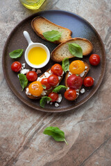 Roasted tomato bruschettas with ricotta and fresh basil, vertical shot on a brown granite background, top view