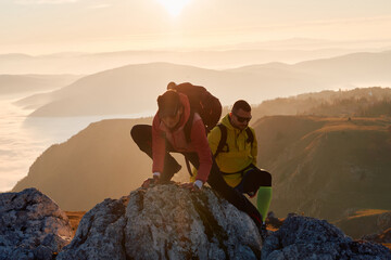 A fit and adventurous couple helps each other climb to the mountain summit during a breathtaking...