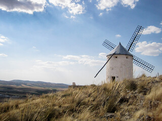 Traditional windmill standing on a grassy hilltop under a clear blue sky. The historic structure...