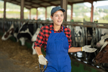 Girl is employee of company during break in work. She stands next to animal pen, with rural hilly...