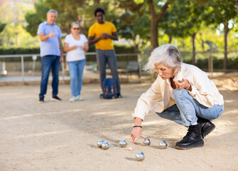 Senior white woman measuring distance between boules in petanque game outside in the park while...