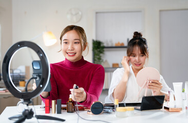 Happy two female bloggers filming video how doing makeup. using phone and tripod. Concept of...