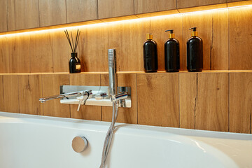 Modern chrome bathtub faucet with shower head mounted on wall with decorative candle and bottles....