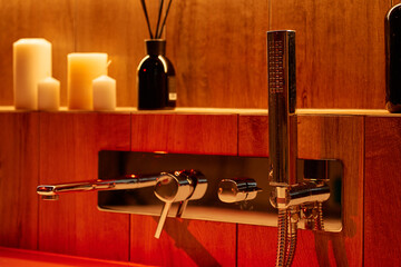 Close-up of chrome bathtub faucet with candles and warm ambient lighting. Concept of relaxation and...