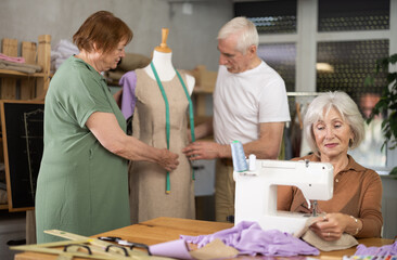 Senior couple work with mannequin at sewing school studio, other female student training to sew ....