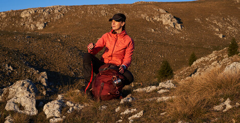 A female hiker unpacks her gear and relaxes after a challenging day of mountain trekking, enjoying...