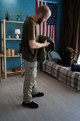 Young bearded man packing sleeping bag for camping going on a hike at home preparing backpack with...