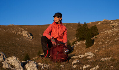 Fototapeta premium A female hiker unpacks her gear and relaxes after a challenging day of mountain trekking, enjoying the tranquility of a sunset