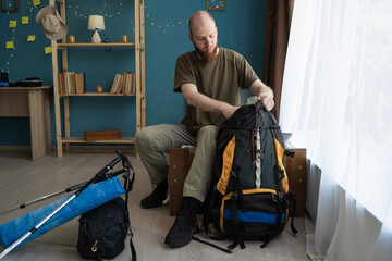 Bearded man packing backpack preparing for hiking trip putting away equipment for mountain trekking