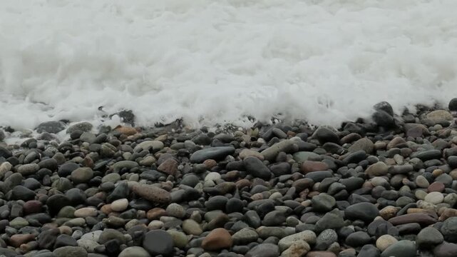 The stormy sky over the rocky seashore on pubble beach with smooth round stones. Waves washing stones on coastline. Slow motion cinematic close up shot. Zen and tranquility concept