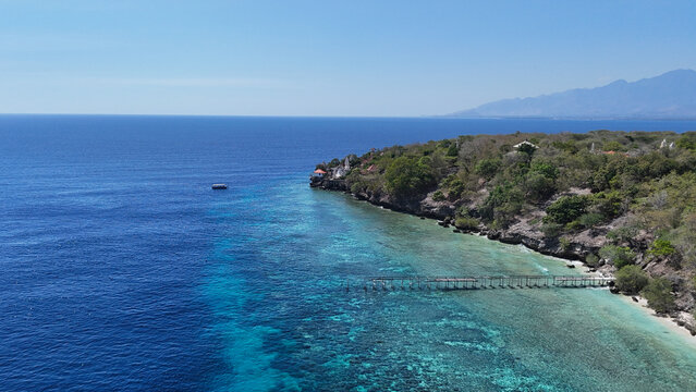 Aerial view Sri Ganesha Temple and a wooden pier stretching into the turquoise sea near a rocky coastline with lush greenery, Menjangan Island, Bali, Indonesia.