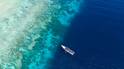 Aerial view of a white boat anchored on the turquoise waters near the shore of Menjangan Island, where snorkelers and divers explore the vibrant coral reefs, Menjangan Island, Bali, Indonesia.