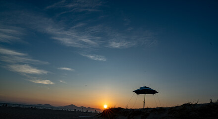 A beautiful beach sunset landscape with a silhouette of a parasol on the sand.