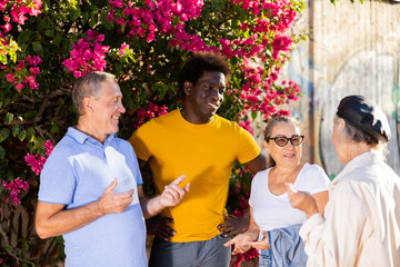 Happy multiracial couples discussing pleasant events among themselves at sunny day in the park