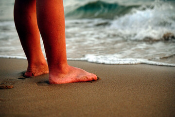 Human feet on a sandy beach at sea at sunset