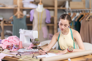 Young woman seamstress drawing sketch on paper in sewing workshop
